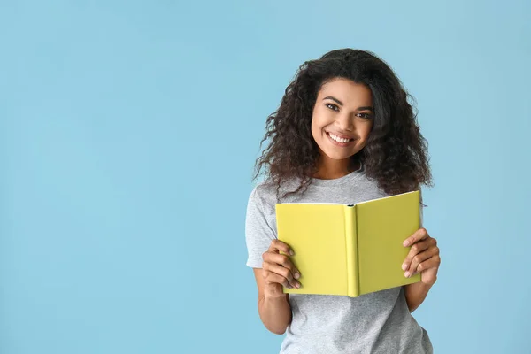 Portrait de femme afro-américaine heureuse avec livre sur fond de couleur — Photo
