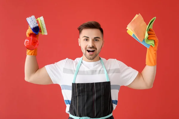 Happy young man with cleaning supplies on color background — Stock Photo, Image