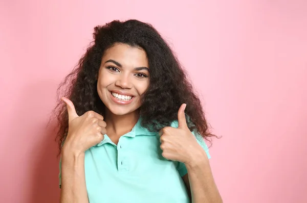 Portrait of happy African-American woman showing thumb-up gesture on color background — Stock Photo, Image