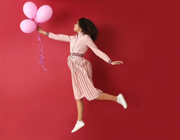 Portret van Jumping Afro-Amerikaanse vrouw met lucht ballonnen op kleur achtergrond — Stockfoto