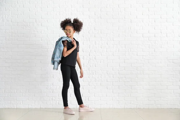 Elegante ragazza afro-americana in jeans vicino al muro di mattoni bianchi — Foto Stock