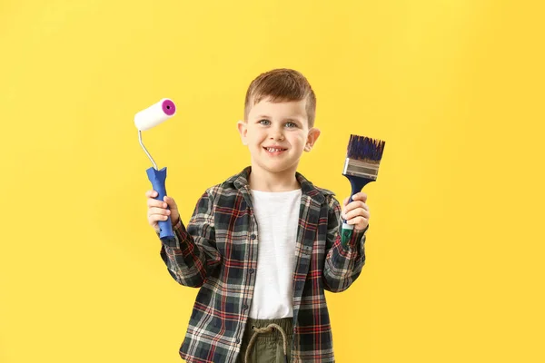 Cute little boy with paint roller and brush on color background — Stock Photo, Image