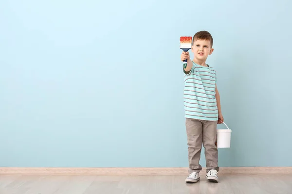 Lindo niño pequeño con cepillo y cubo de pintura cerca de la pared de color — Foto de Stock