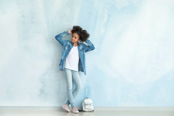 Stylish African-American girl in jeans clothes and with backpack near color wall — Stock Photo, Image