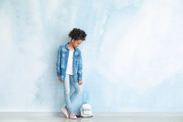 Stylish African-American girl in jeans clothes and with backpack near color wall