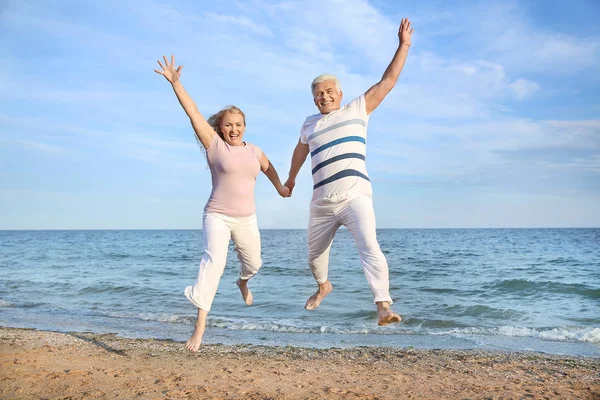 Happy jumping mature couple at sea resort — Stock Photo, Image