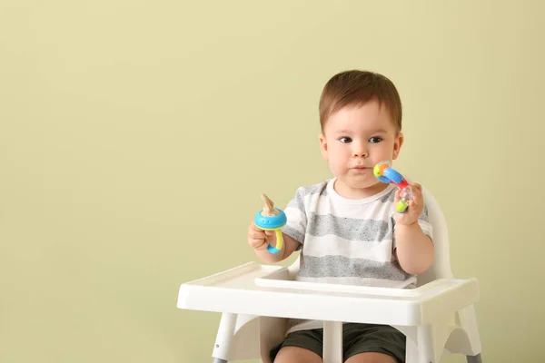 Cute little boy with nibbler sitting in high chair against color background — Stock Photo, Image