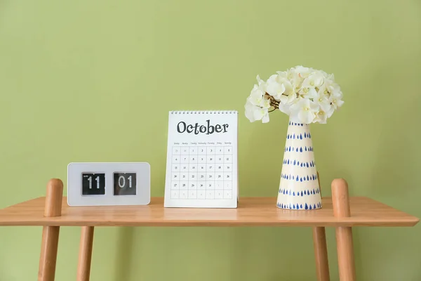 Flip calendar with alarm clock and flowers in vase on table in room