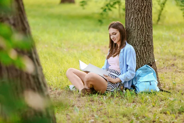 Vacker kvinnlig student sitter underträd i parken — Stockfoto