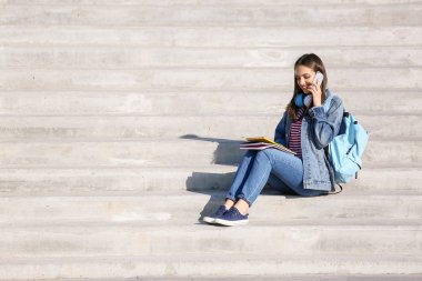 Açık havada merdivenlerde otururken telefonda konuşan güzel kadın öğrenci
