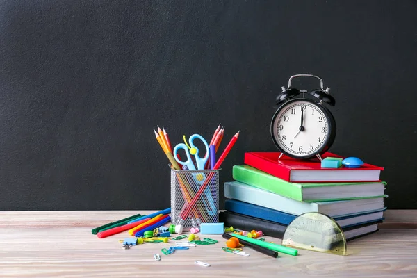 Set of school supplies and clock on table in classroom — Stock Photo, Image