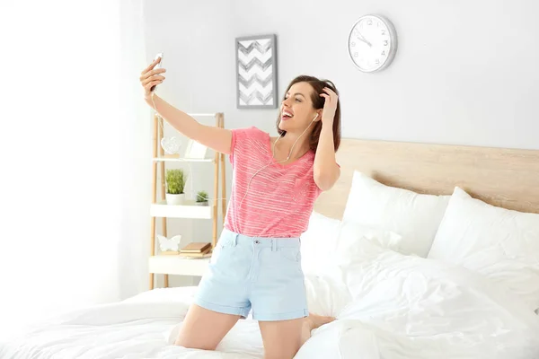 Mooie jonge vrouw die plezier heeft tijdens het luisteren naar muziek in de slaapkamer — Stockfoto