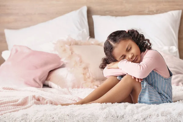 Sad little African-American girl sitting on bed — Stock Photo, Image