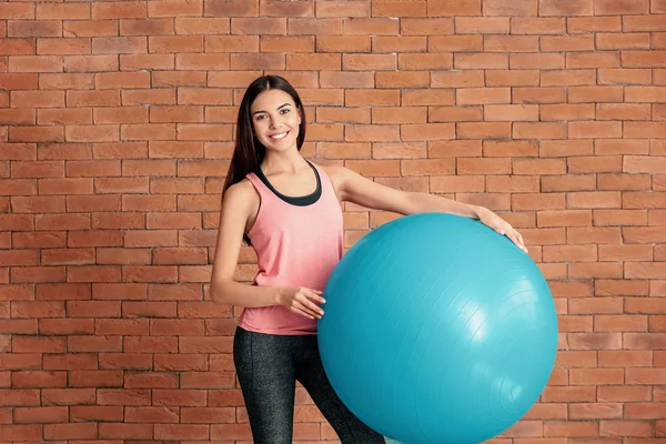 年轻的运动女人与健身球附近的砖墙 — 图库照片