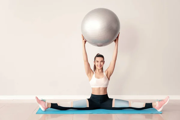 Jovem mulher esportiva com fitball fazendo exercícios perto da parede leve — Fotografia de Stock