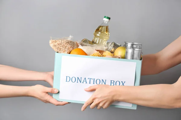 Добровольцы дают коробку с кормом для бедных женщин на сером фоне — стоковое фото