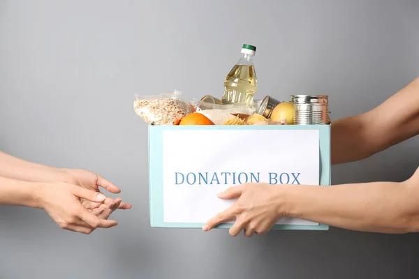 Caja de donaciones de voluntarios con alimentos de donación a mujeres pobres sobre fondo gris — Foto de Stock