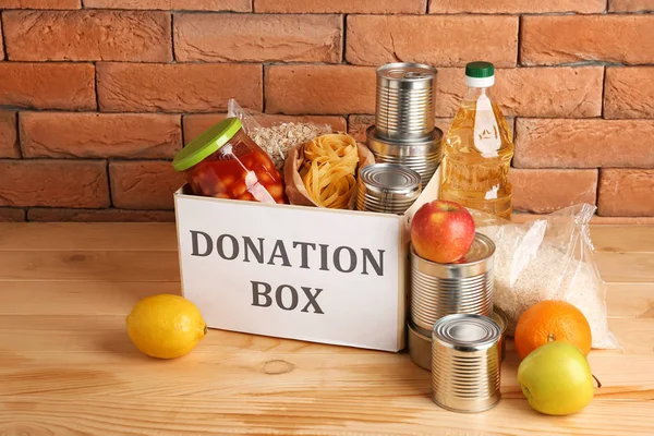 Caja con comida de donación en la mesa cerca de la pared de ladrillo — Foto de Stock