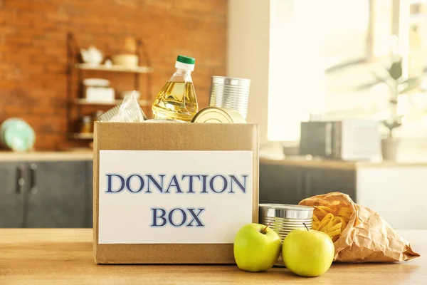 Box with donation food on table in kitchen