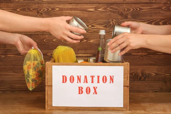 Vrijwilligers zetten voedsel in donatie doos op houten achtergrond Stockfoto