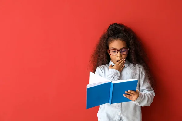 Sorprendida chica afroamericana con libro sobre fondo de color — Foto de Stock