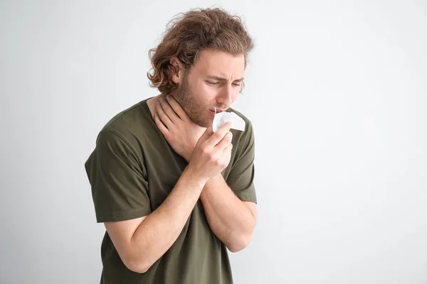 Sick young man with nose wiper on light background — Stock Photo, Image