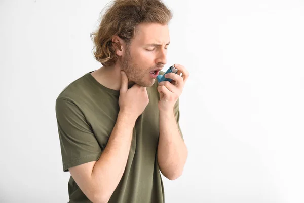 Homem jovem com inalador tendo ataque de asma em fundo claro — Fotografia de Stock