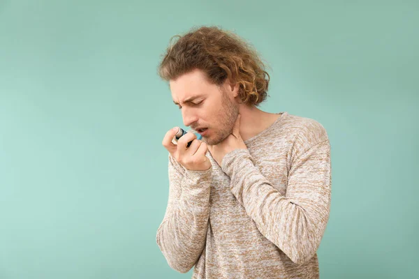 Young man with inhaler having asthma attack on color background — Stock Photo, Image