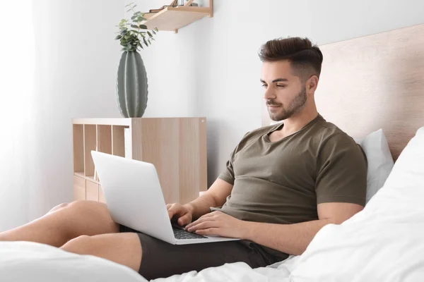 Handsome man with laptop resting in bedroom — Stock Photo, Image