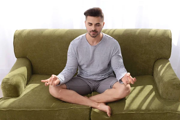 Handsome man meditating on sofa at home