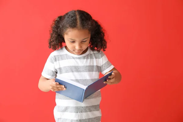 Retrato de adorable niña afroamericana leyendo libro sobre fondo de color — Foto de Stock