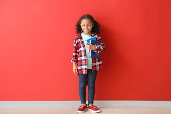 Portrait of adorable little African-American girl with books near color wall — Stock Photo, Image