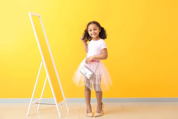 Retrato de adorable niña afroamericana usando zapatos de madre cerca de la pared de color — Foto de Stock
