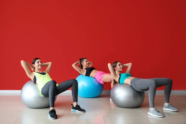 Jóvenes mujeres deportivas con pelotas haciendo ejercicios cerca de la pared de color —  Fotos de Stock