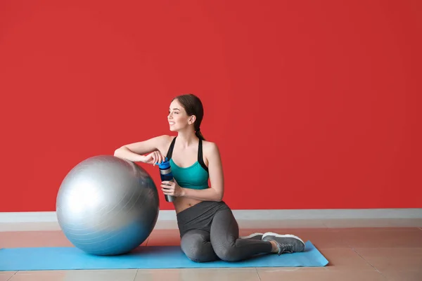 年轻的运动女人与健身球和瓶水附近的彩色墙 — 图库照片