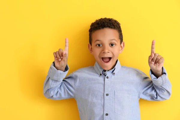 Cute African-American boy pointing at something on color background — Stock Photo, Image