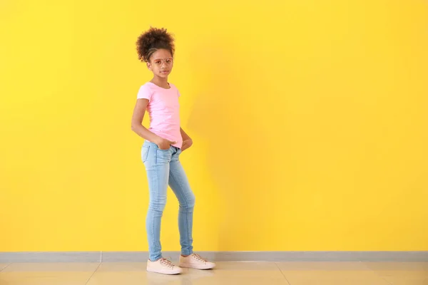 Stylish African-American girl in jeans near color wall