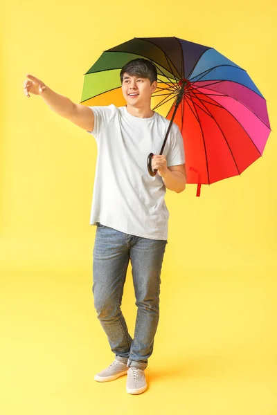 Handsome Asian man with umbrella on color background — Stock Photo, Image