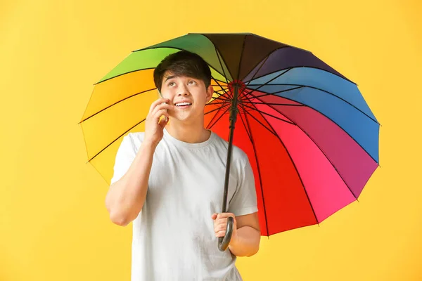 Bel homme asiatique avec parapluie parler par téléphone sur fond de couleur — Photo