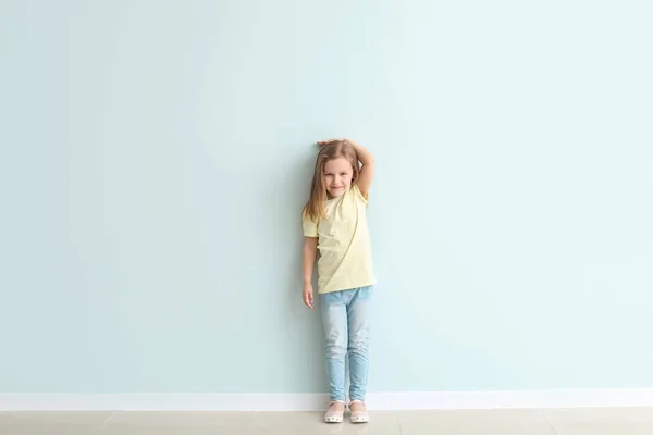 Cute little girl measuring her height near wall — Stock Photo, Image