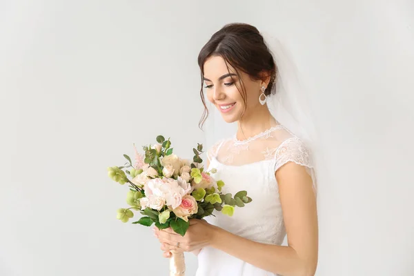 Mooie jonge bruid met boeket bloemen op lichte achtergrond — Stockfoto