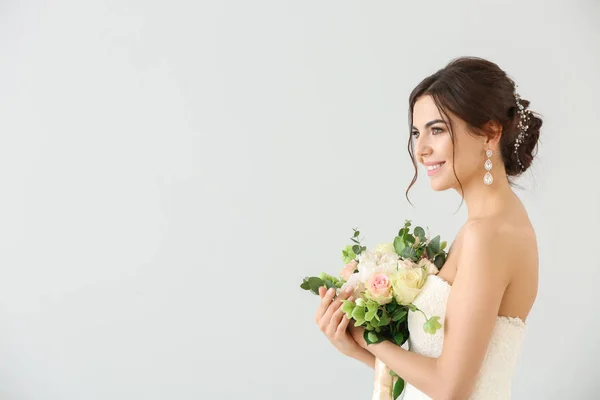 Mooie jonge bruid met boeket bloemen op lichte achtergrond — Stockfoto