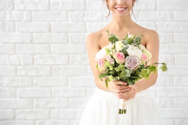 Hermosa novia joven con ramo de flores sobre fondo de ladrillo blanco —  Fotos de Stock