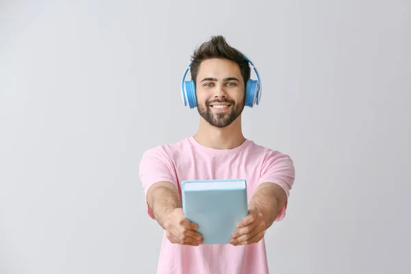 Young man listening to audiobook on light background — Stock Photo, Image