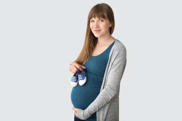 Giovane donna incinta con scarpe bambino su sfondo chiaro — Foto Stock