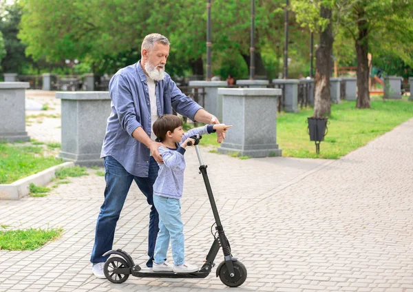 Lindo niño pequeño con abuelo montando patinete scooter en el parque —  Fotos de Stock