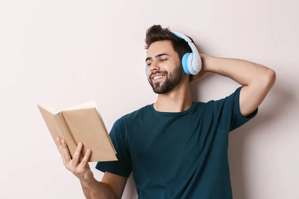 Jonge man luisteren naar muziek en lezen boek op lichte achtergrond — Stockfoto