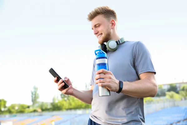 Joven deportivo con teléfono móvil y botella de agua en el estadio — Foto de Stock