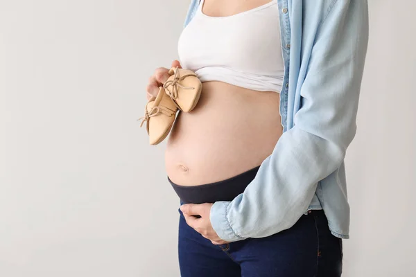 Молодая беременная женщина в детской обуви на светлом фоне — стоковое фото