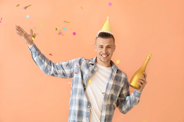 Drunk man with party hat and bottle of champagne on color background — Stock Photo, Image